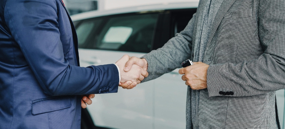 Men shaking hands in front of car